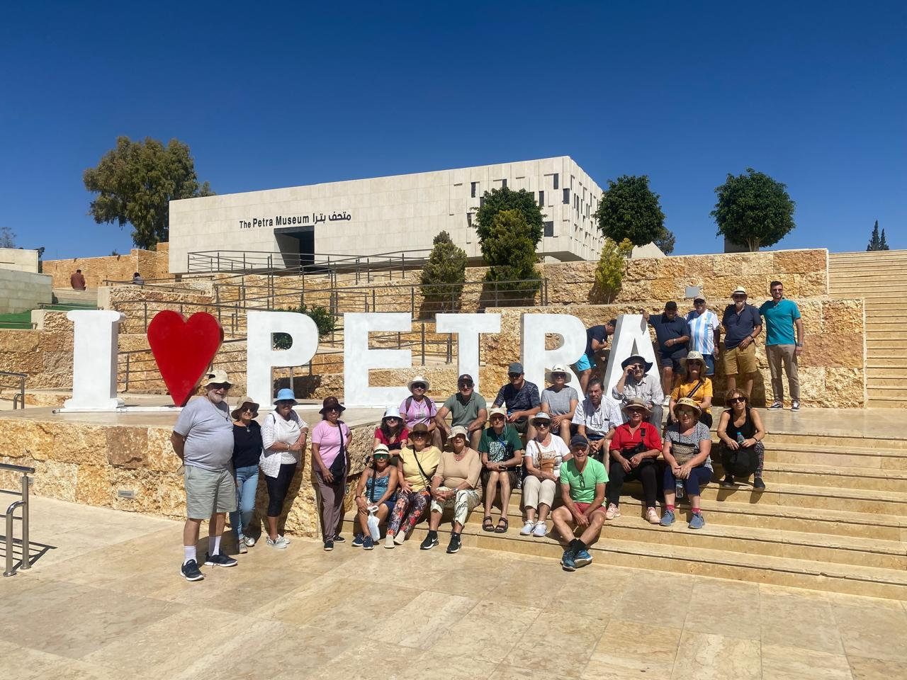 A group of tourists posing and smiling in front of the ‘I Love Petra’ sign, celebrating their visit to the iconic site